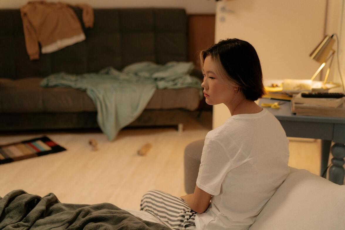 Woman sitting on the floor of a cluttered living room, looking overwhelmed and emotionally drained, representing the emotional weight behind procrastination.