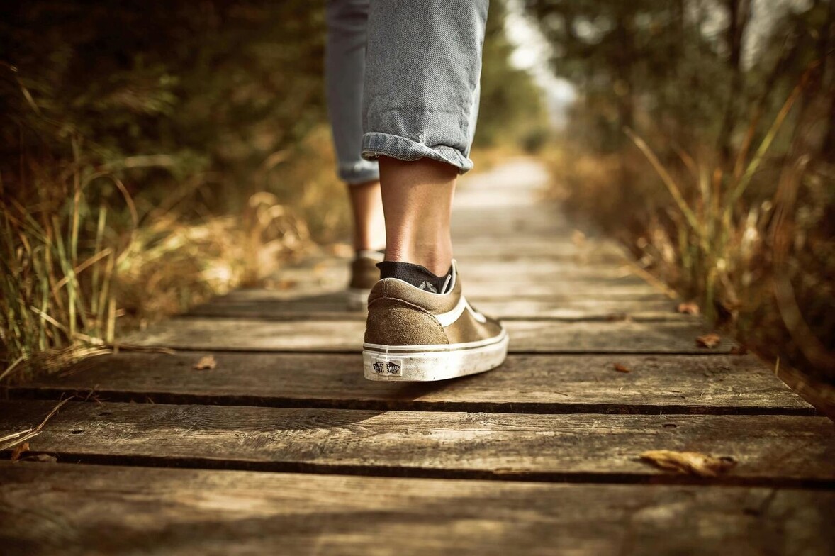 Close-up of a woman’s feet in running shoes walking along a nature trail, symbolizing steady progress, personal growth, and consistency in therapy.
