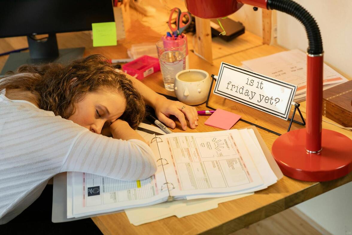 Overwhelmed woman at her desk, feeling drained from overcommitment.