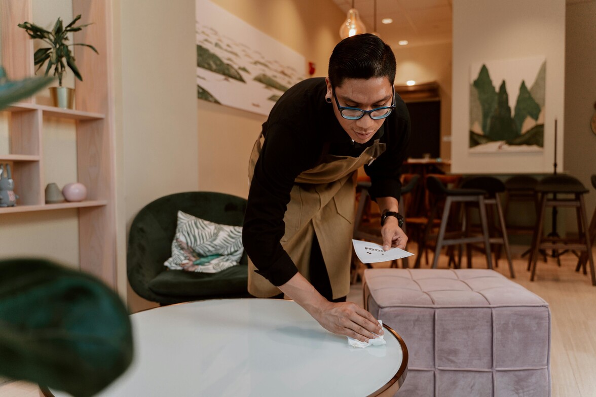 Woman wiping a coffee table in a living room that is already immaculately neat and clean—representing how seemingly ordinary routines, like cleaning, can be a way anxiety shows up in daily life.