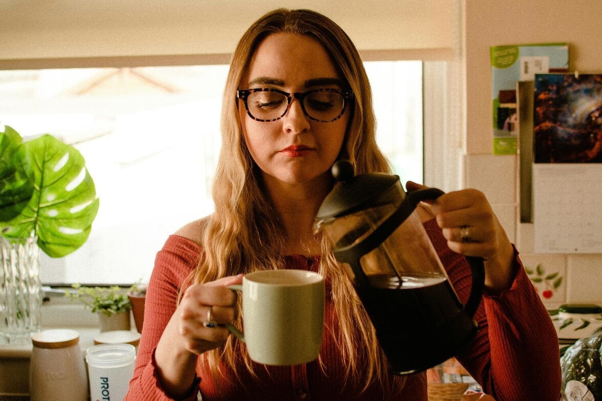 A woman in a softly lit kitchen pours herself a cup of coffee, taking a quiet moment of self-care while coping with mental and emotional overload.